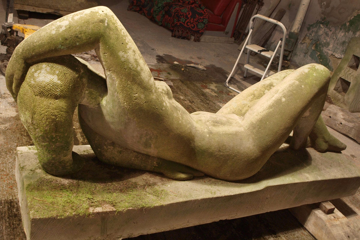 Skulptur einer liegenden Frau aus Sandstein vor der Restaurierung überzogen mit Moos Rückenansicht