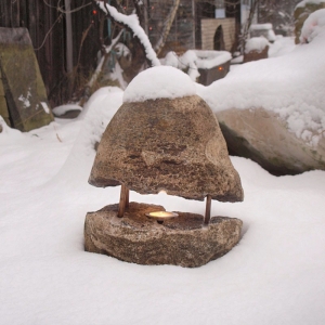 Lampe aus Findling mit brennender Kerze draußen im Schnee