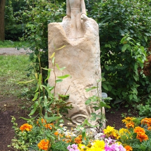Grabstein als Stele aus hellem Sandstein in Form des kleinen Prinzen mit Blumenschmuck