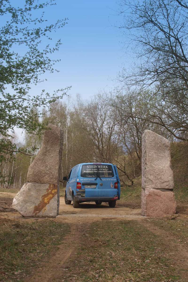 Tor auf freiem Feld im Geopark aus zwei hohen Steinen mit blauem Bus