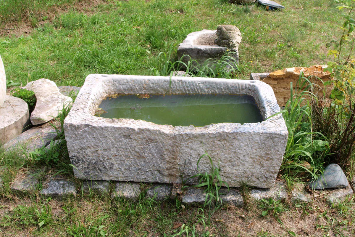 Großer Steintrog aus hellem Kalkstein gefüllt mit grünlichem Wasser